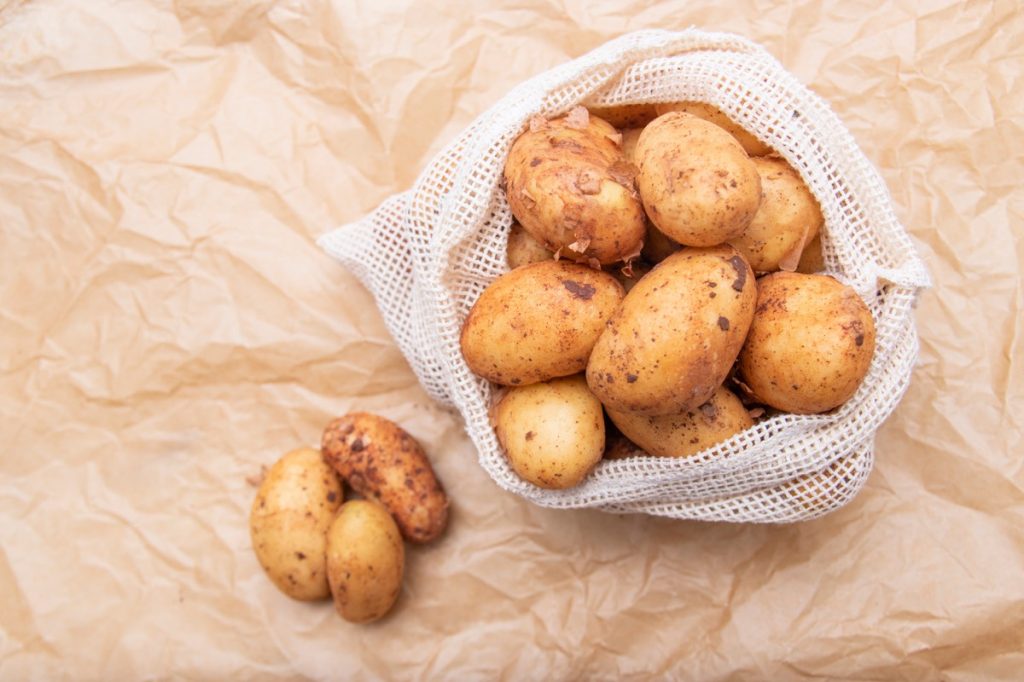 Raw fresh organic potatoes. Full bag of potatoes. Burlap sack with potatoes. Space for text,