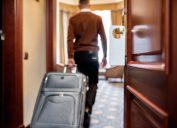 Cropped shot of middle-aged businessman in casual wear with suitcase entering his room in the background. A door with a sign at the front. Horizontal shot. Selective focus