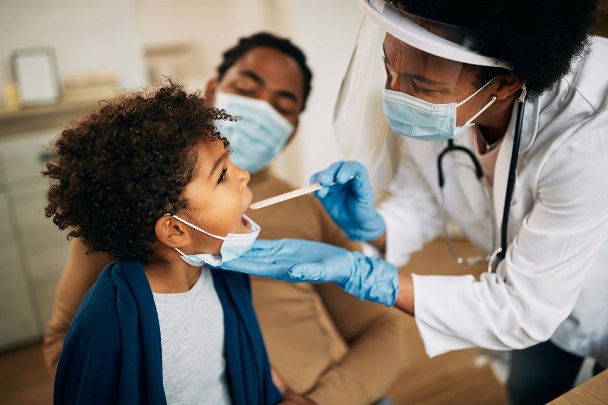 Family doctor examining a little boy's throat while visiting him at home during the coronavirus pandemic.