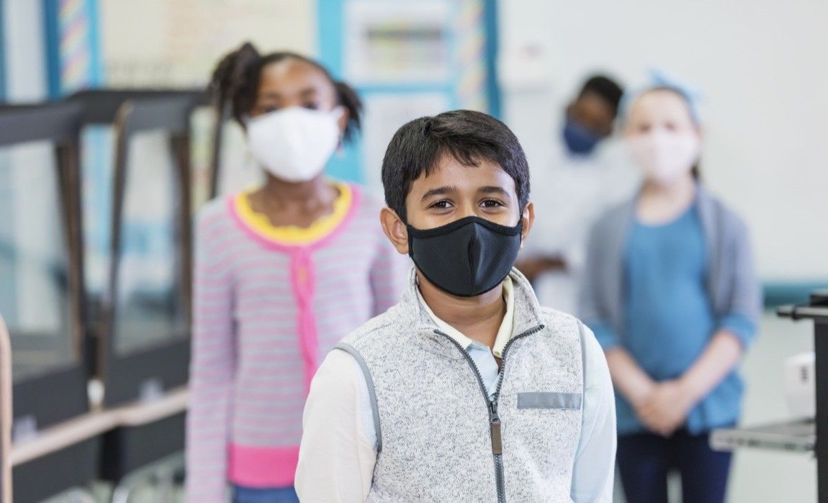 group of elementary school students in the classroom during the covid-19 pandemic, wearing face masks and standing six feet apart, social distancing.