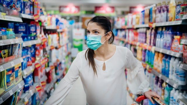 Woman wearing protective mask preparing for virus pandemic spread quarantine.Finding the right products on the shelves in the supermarket.Hygiene, cleaning and disinfection products.Budget buying.
