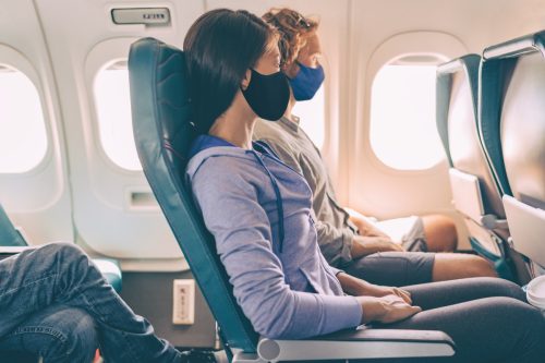 Tourist couple wearing masks on travel vacation flight inside airplane.  Coronavirus safety prevention for flight passengers.  People lifestyle.