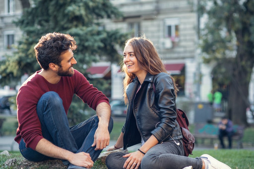 A young couple on a date sitting in a park chatting with each other and smiling