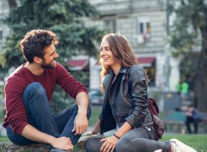 A young couple on a date sitting in a park chatting with each other and smiling