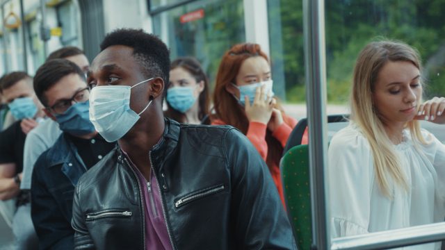 Blonde woman sneezes inside public tram. Scared people passengers immediately wearing face masks for virus prevention.