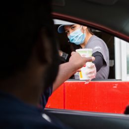 A man reaches for his food at the McDonalds drive-thru window as the employee wears a mask for protection.