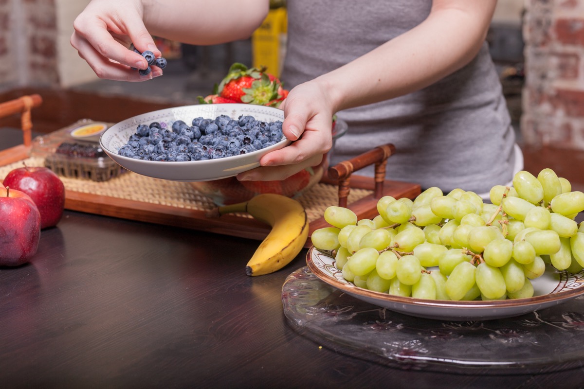 person with plates of grapes and blueberries in kitchen