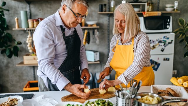 Senior men and women cutting fresh raw vegetable in kitchen
