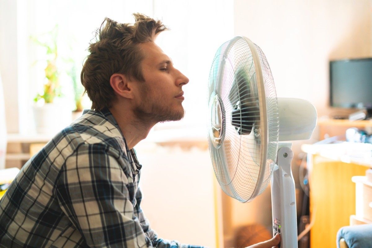 person enjoying electric fan, cooling his face at home, during summer heat