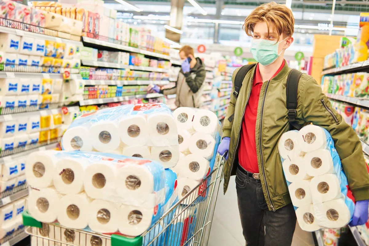 man in mask and protective gloves buying toilet paper in shop. Panic at coronavirus epidemic