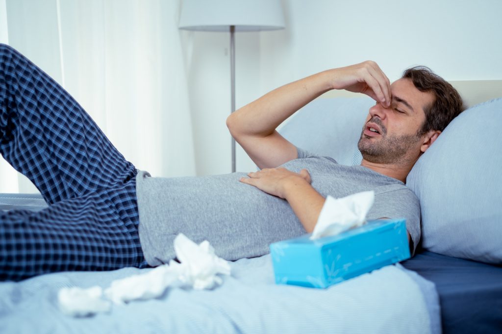 A man lying in bed sick with COVID symptoms and surrounded by tissues