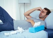 A man lying in bed sick with COVID symptoms and surrounded by tissues