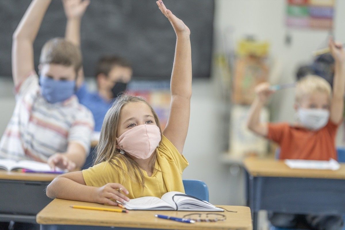 Group of students wearing protective masks while raising their hands in class.