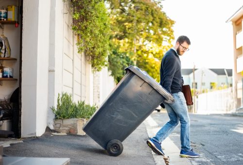 Man pulling a wheeled dumpster out of his garage while going to work