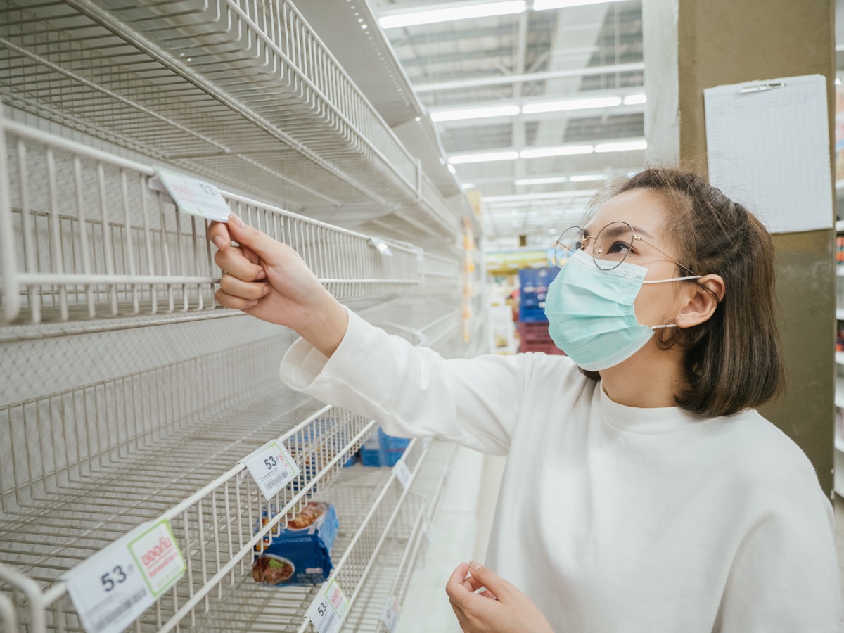 woman wearing mask and reading label on empty shelf in Supermarket in Bangkok, Thailand.
