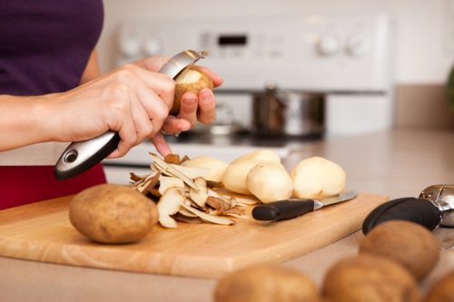 Color image of a young woman peeling potatoes in the kitchen of her home.