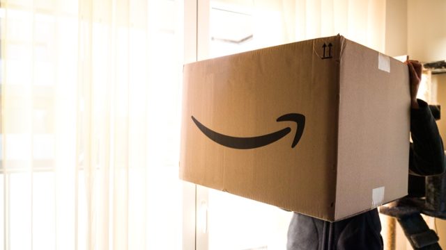 person holding large amazon prime box in well-lit room