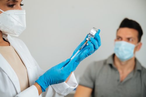 Tăiați un medic anonim în mănuși care umple o seringă cu vaccinul COVID 19 împotriva unui pacient adult discret din spital