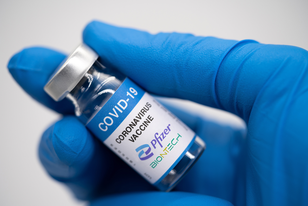 A gloved hand holding a vial of Pfizer BioNTech COVID-19 vaccine