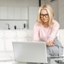 Brooding middle-aged woman using a laptop for remote work at home, studying online, a serious female mature teacher checking tasks on the computer