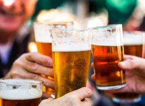 Close up color image depicting a group of people celebrating with a toast. The people cheers their glasses of beer (pints of beer) together in a gesture of celebration, togetherness and happiness. The people are defocused in the background, while focus is on the glasses of beer in the foreground. Room for copy space.
