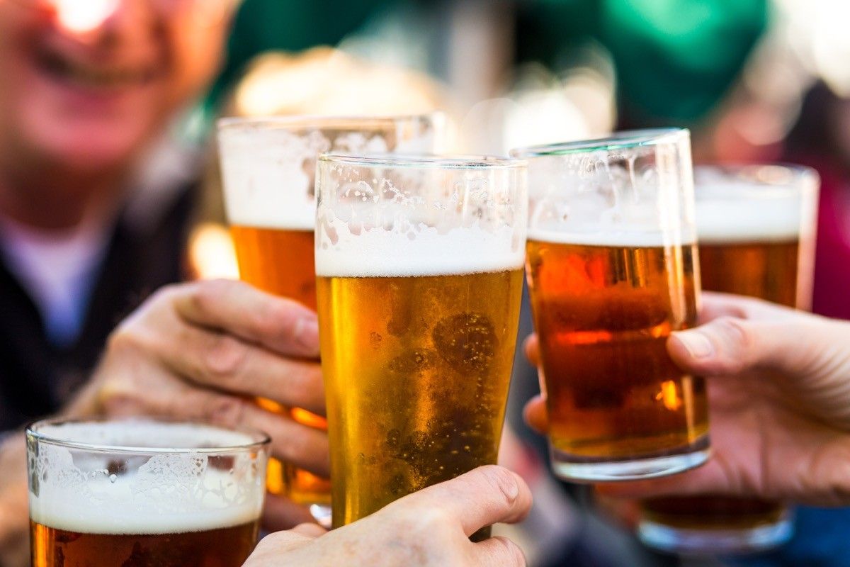 Close up color image depicting a group of people celebrating with a toast. The people cheers their glasses of beer (pints of beer) together in a gesture of celebration, togetherness and happiness. The people are defocused in the background, while focus is on the glasses of beer in the foreground. Room for copy space.