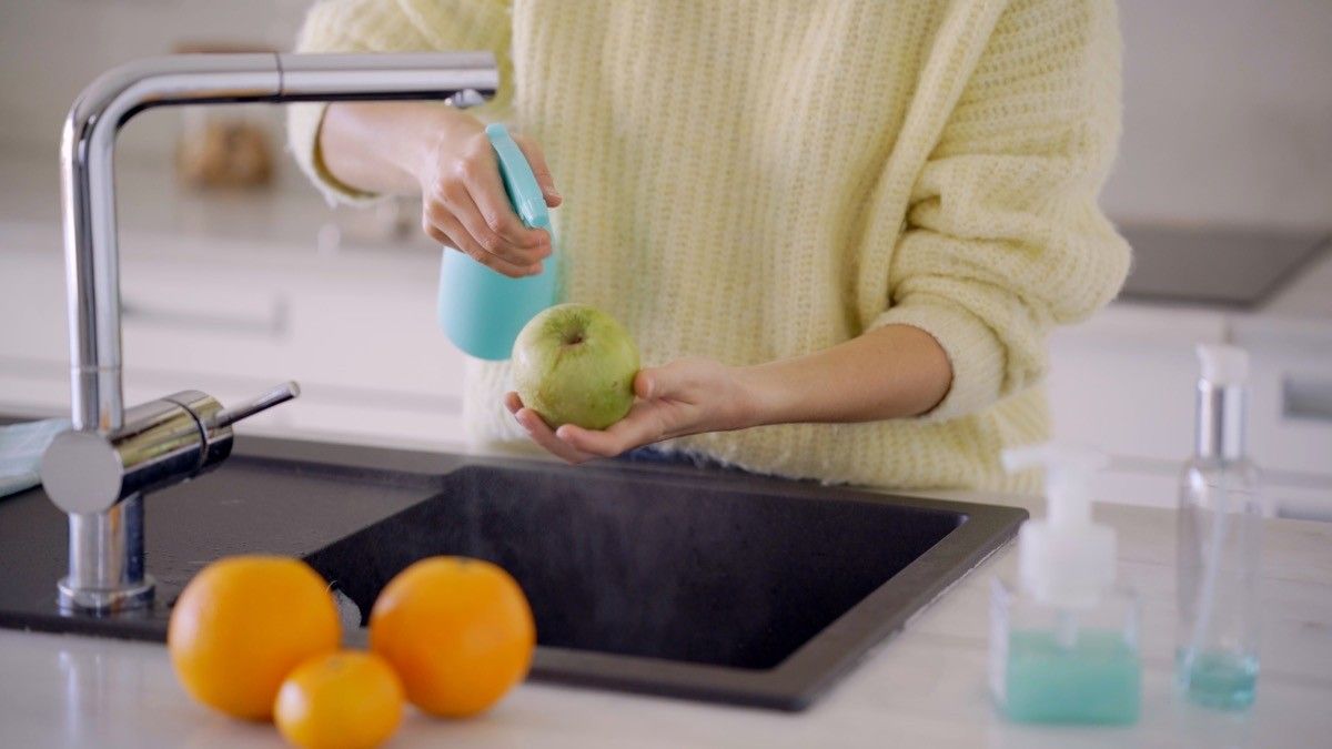 person spraying cleaning solution on fruit at the sink