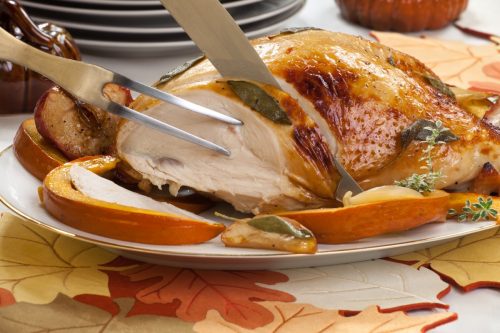 Sage - honey butter rub turkey breast garnished with roasted pumpkin and apples in fall themed surrounding.