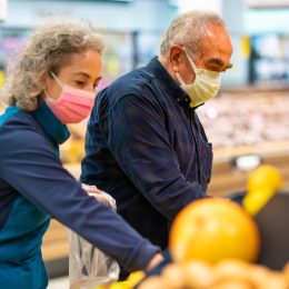 The senior couple that goes shopping with protective face masks selects fruit and vegetables and fills them into shopping bags