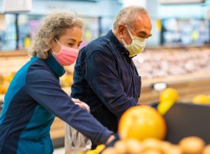 The senior couple that goes shopping with protective face masks selects fruit and vegetables and fills them into shopping bags