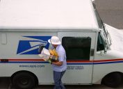 A mail carrier bringing boxes and envelopes from inside a mail truck