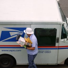 A mail carrier bringing boxes and envelopes from inside a mail truck