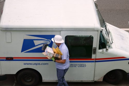A mail carrier bringing boxes and envelopes from inside a mail truck