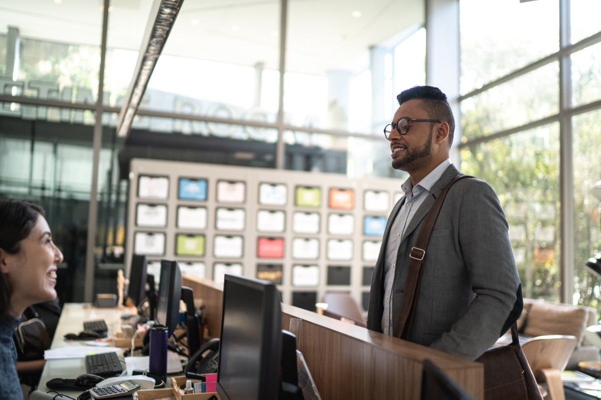 Man in an office reception / lobby talking to a secretary