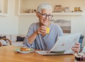 A senior woman drinking juice at breakfast while reading the paper