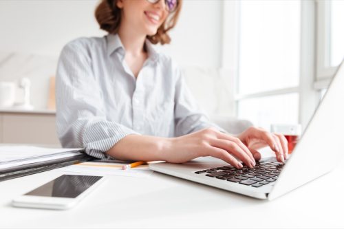 Foto cropped de mulher morena bonita digitando e-mail no computador portátil enquanto senta em casa, foco seletivo na mão