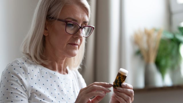 A senior woman holding a pill bottle while reading the label