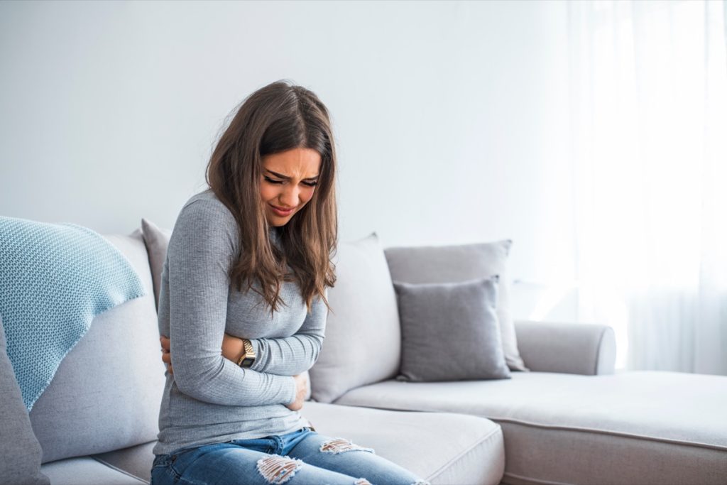 young woman in gray shirt and jeans with stomach pain on couch
