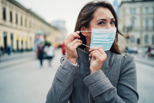 A young woman putting on a face mask while walking down the street