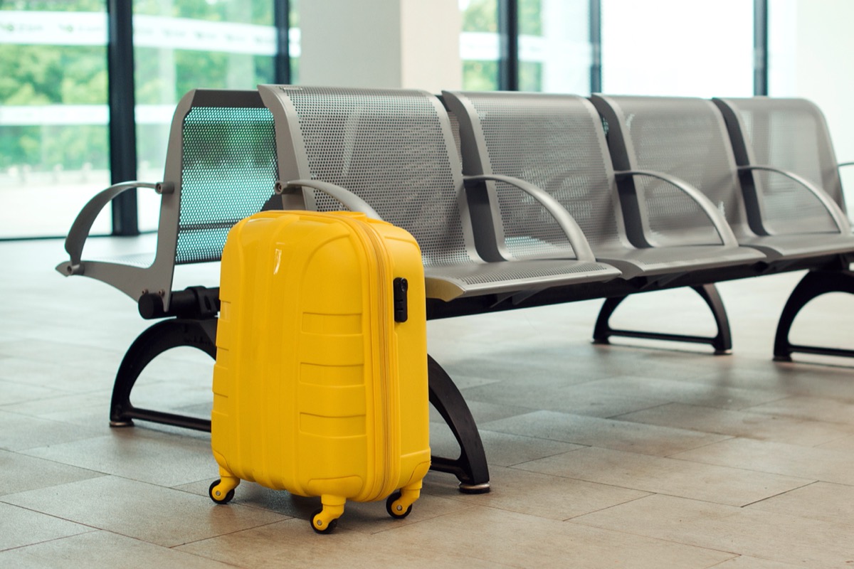 yellow hard-sided suitcase alone at airport