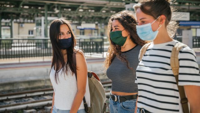 A group of young women walking through an outdoor train station while wearing masks