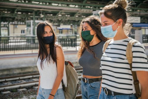 A group of young women walking through an outdoor train station while wearing masks