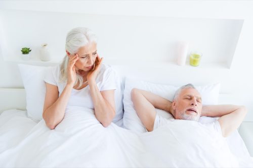 Older couple in bed, woman awake looking annoyed at man