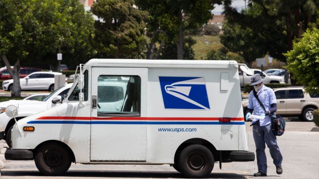 Fullerton, California / USA - August 13, 2020: A USPS (United States Parcel Service) mail truck and postal carrier make a delivery.