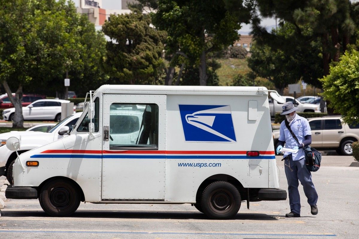 Fullerton, California / USA - August 13, 2020: A USPS (United States Parcel Service) mail truck and postal carrier make a delivery.