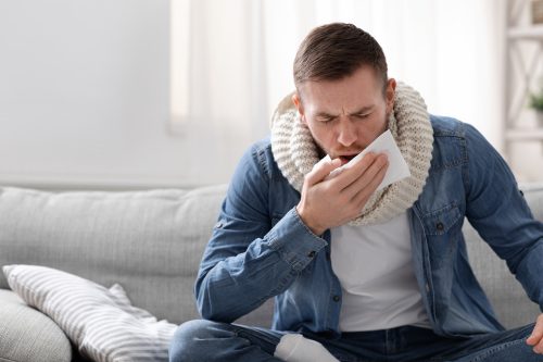 Young man coughing into a napkin