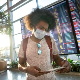 male traveler wearing a facemask at the airport with the flight schedule