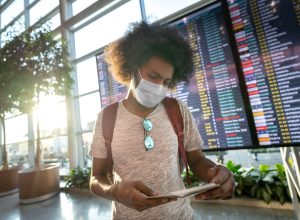 male traveler wearing a facemask at the airport with the flight schedule