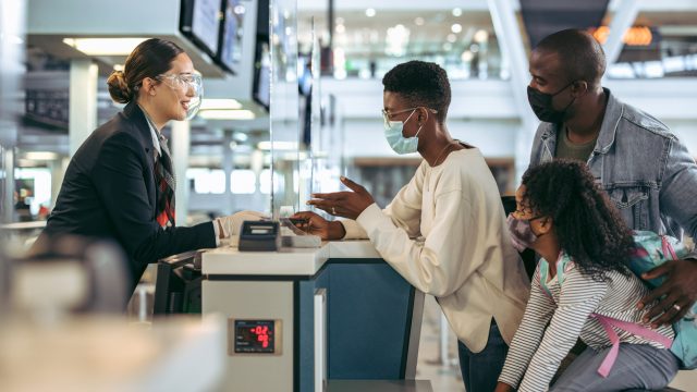 A family wearing face masks speaks with a ticket agent at the airport