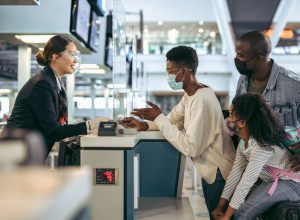A family wearing face masks speaks with a ticket agent at the airport
